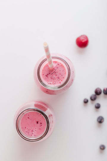 Two pink smoothies in jars with straws on a white background, surrounded by berries.
