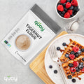 A white plate with two waffles with berries and powdered sugar, alongside a fork on a wooden board & with A bag of Quay Naturals Premium Tigernut Flour and a bowl of berries.