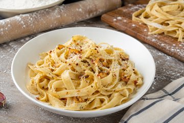 Gluten-free fresh pasta with garlic brown butter, grated Parmesan, and herbs in a white bowl